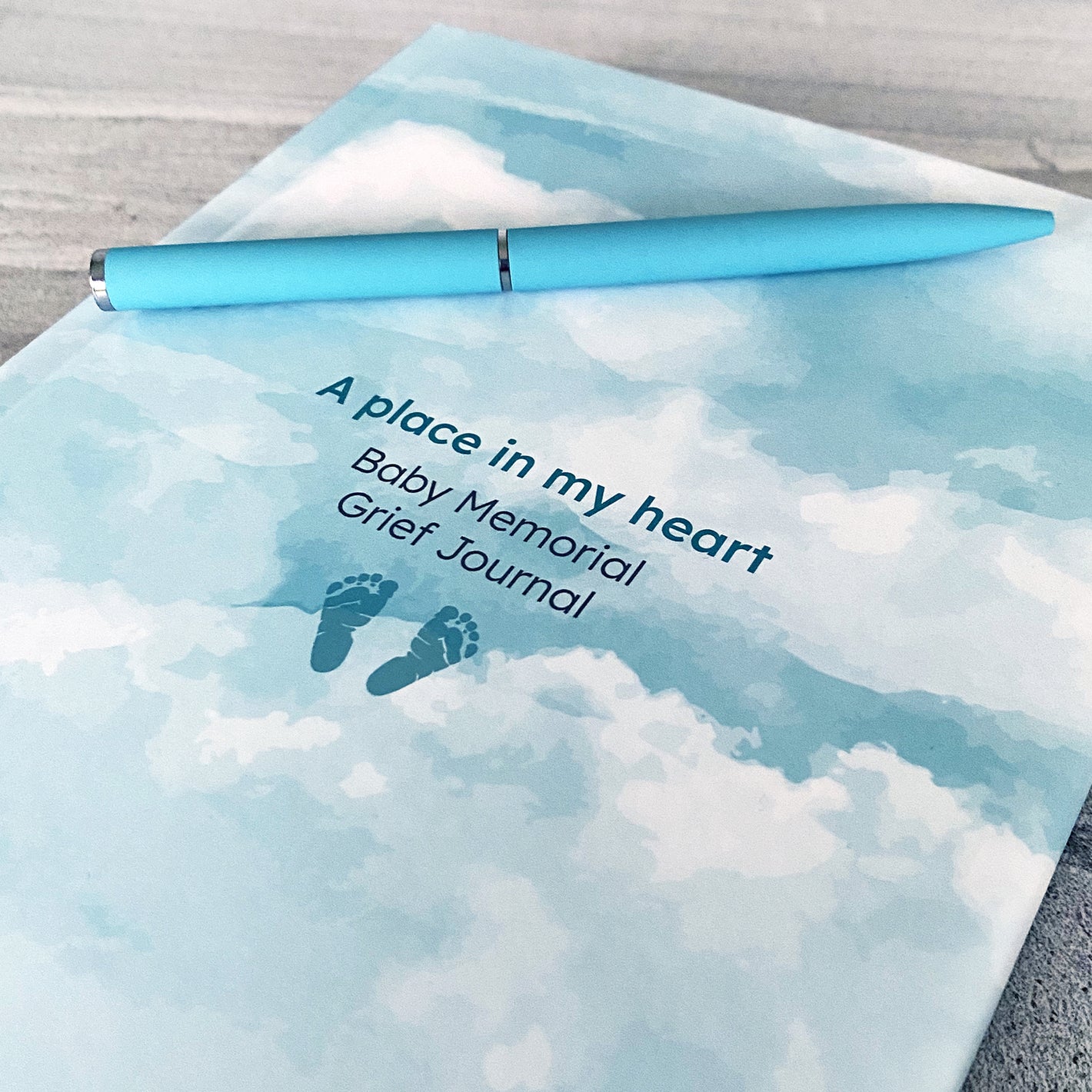 Front of baby memorial grief journal with footprints and sky design with a matching pen
