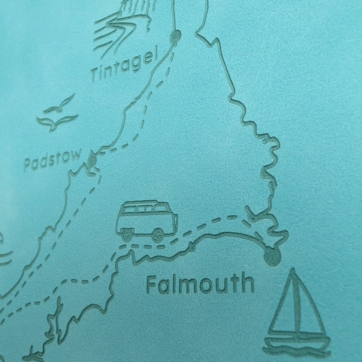 Detailed engraving on a turquoise Cornwall road trip journal showing Tintagel, Padstow, Falmouth and a miniature campervan.