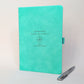 Personalised turquoise retirement journal with engraved “Goodbye work, hello freedom”, compass design and custom name, shown with a silver metal pen.