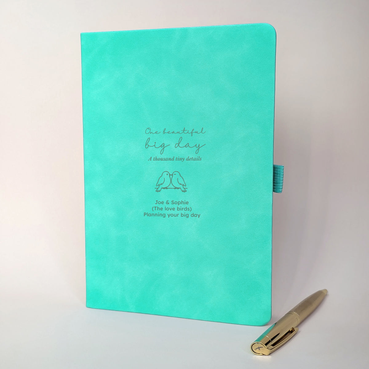 Turquoise personalised engagement journal with engraved love birds design, names Joe and Sophie, “Planning your big day” wording and coordinating gold metal pen.