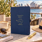 Personalised navy Australia travel journal with gold foil map and flight path, styled on a travel table with Sydney Opera House in the background.co