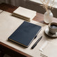 Personalised navy work notebook and pen with name and Creative Director job title, styled on a desk with coffee and stationery, ideal as a new job or promotion gift.