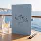 A lifestyle image onboard a cruise ship of a light blue journal showing 6 destinations on a Mediterranean cruise , personalised with black foil.  Sea and cliffs are in the background