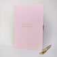 Pink personalised A5 work journal with Olivia Hughes and Events Coordinator on the cover in gold, with matching gold pen. Personalised notebook gift for a colleague, employee or new job.