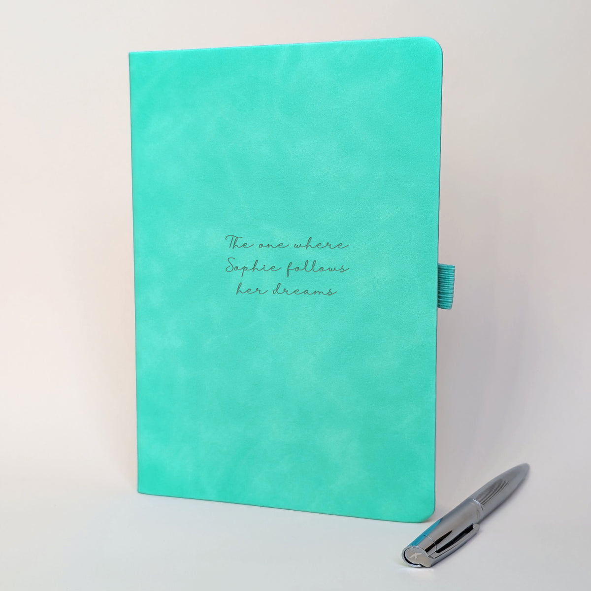 Turquoise personalised journal with matching silver pen featuring “The one where Sophie follows her dreams”, showing how the journal can be customised for a new beginning, achievement or exciting life change.