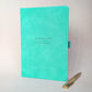 Turquoise personalised A5 journal with Benjamin Clarke and Graphic Designer on the cover, shown with a metal pen. Personalised name and job title notebook for work, a new role or colleague gift.