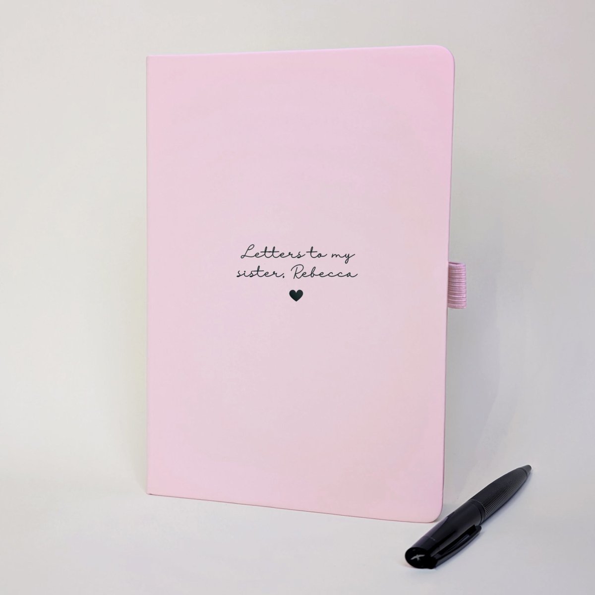 Personalised pink grief journal for a sister, with black foiled “Letters to my sister, Rebecca” wording, heart detail and matching black metal pen.