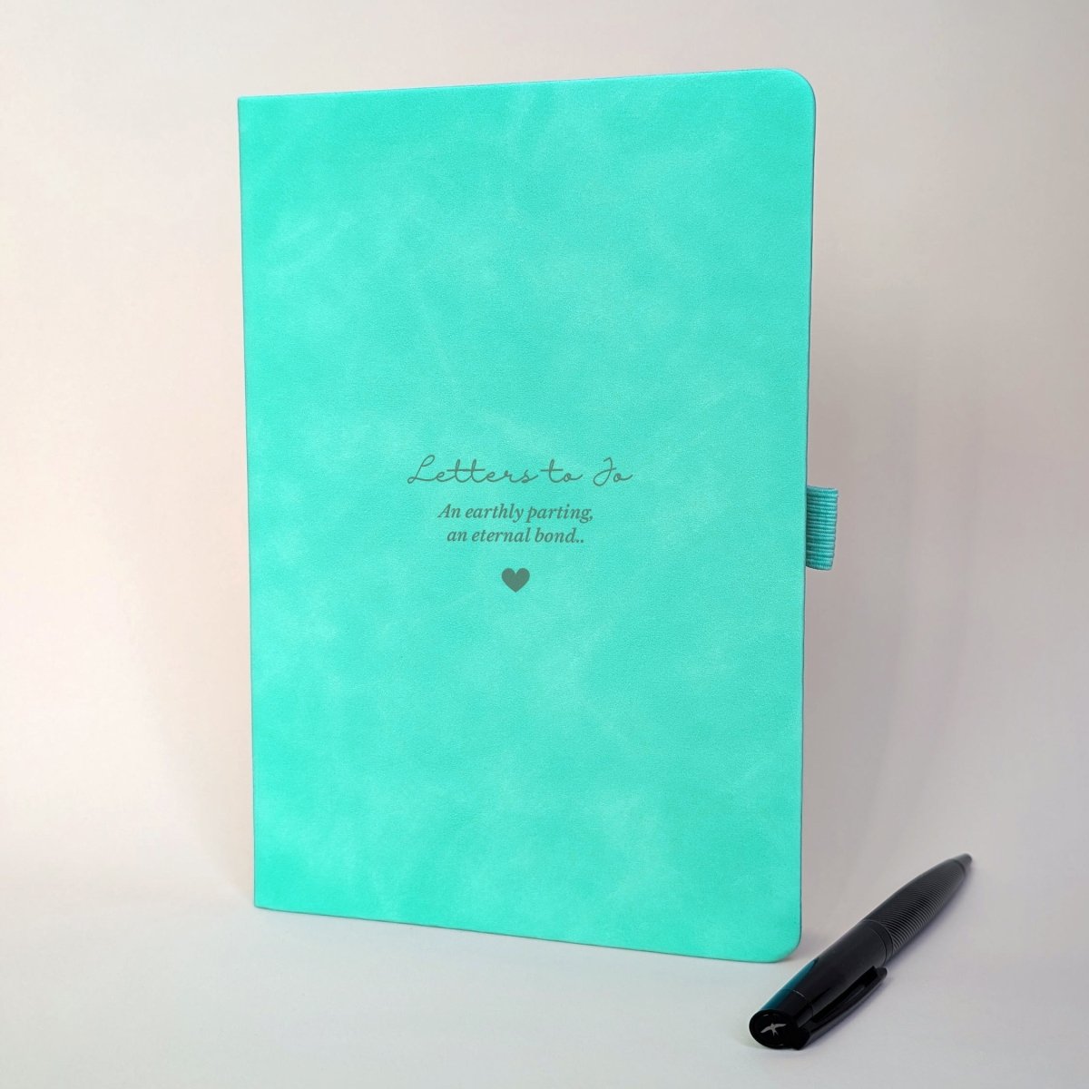 Personalised turquoise grief journal with “Letters to Jo” and remembrance wording, engraved onto the cover and shown with a black metal pen.