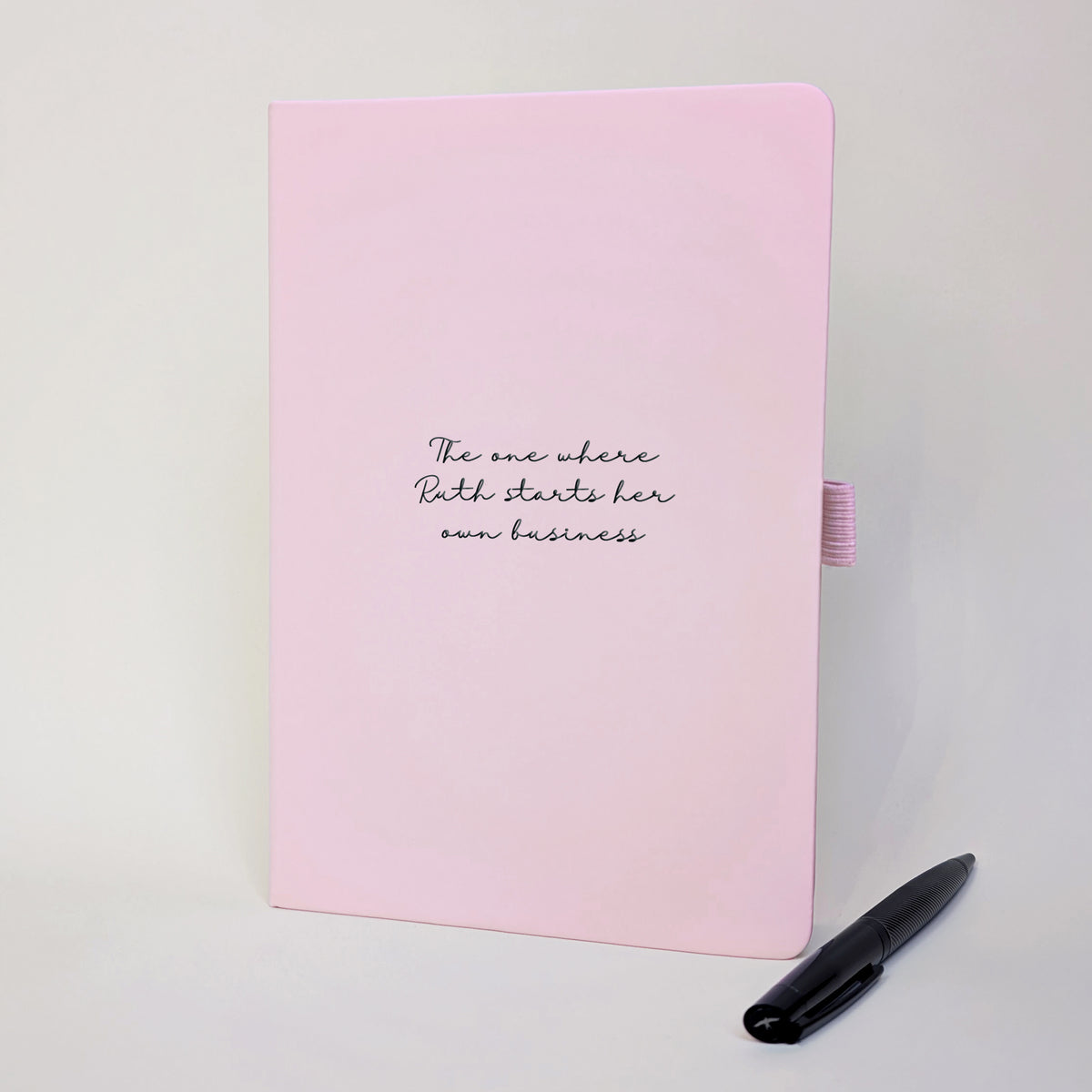 Pink personalised journal with black pen featuring “The one where Ruth starts her own business”, a custom new business gift for celebrating a business launch, career change or new chapter.