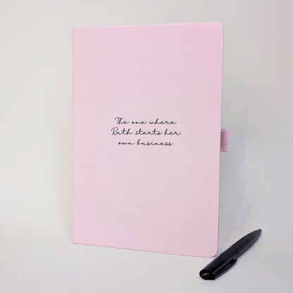 Pink personalised journal with black pen featuring “The one where Ruth starts her own business”, a custom new business gift for celebrating a business launch, career change or new chapter.