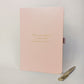 Blush pink personalised journal and gold pen with the cover wording “The one where mum also became nan”, shown as a keepsake gift idea for a new grandmother or family milestone.