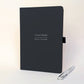 Personalised black A5 work journal with Daniel Foster and Project Manager on the cover, shown with a silver metal pen. A thoughtful personalised gift for a colleague, new job, promotion or work milestone.