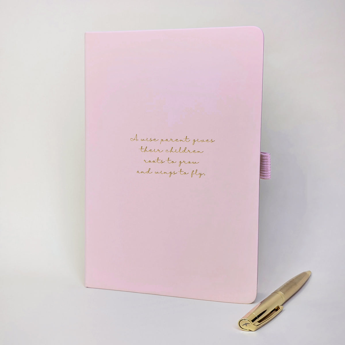 Light pink personalised quote notebook with gold foil text reading “A wise parent gives their children roots to grow and wings to fly.” shown with a gold pen.