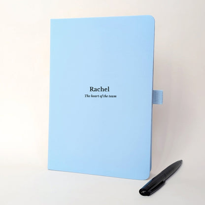 Pale blue personalised staff appreciation journal for Rachel reading “The heart of the team”, shown with a black pen.