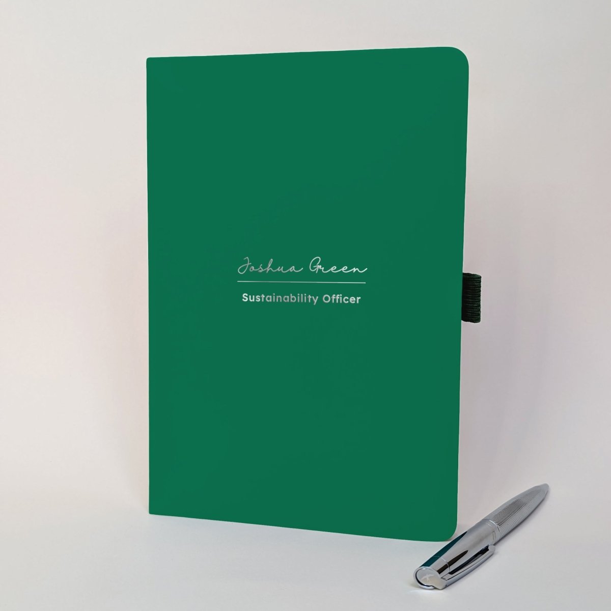 Green personalised A5 journal with Joshua Green and Sustainability Officer on the cover in silver, shown with a matching silver metal pen. Personalised name and job title notebook for work, a new role or colleague gift.